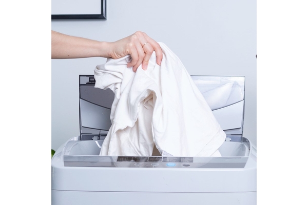 A hand placing a white shirt into a laundry machine.